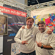 Graffiti-Künstler Markus Genesius und ein Mitarbeiter eines Malerbetriebs an einem Messestand